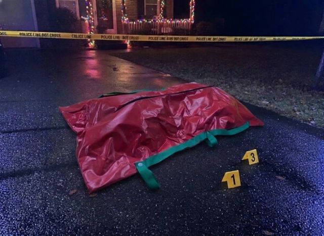 The red bag zipped shut on a wet driveway at night, behind police tape, with yellow evidence markers.